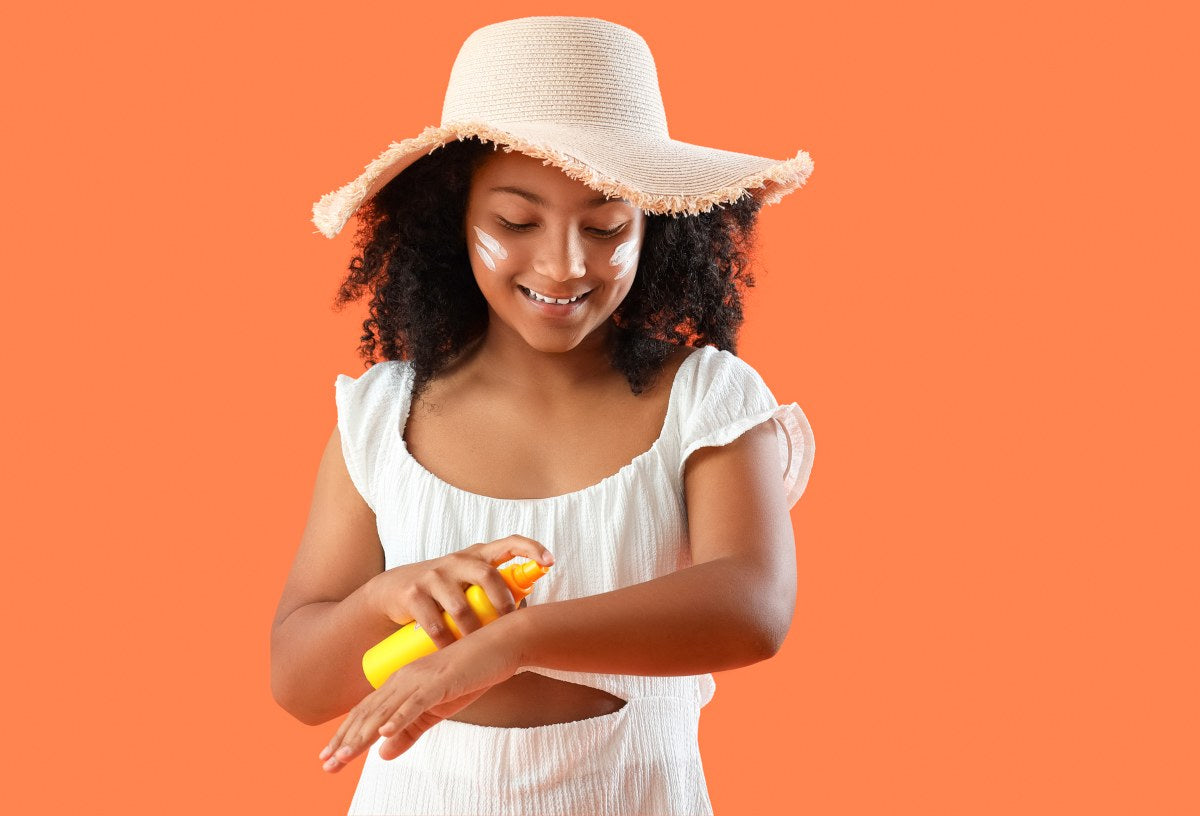 Little African American girl applying sunscreen cream on orange background