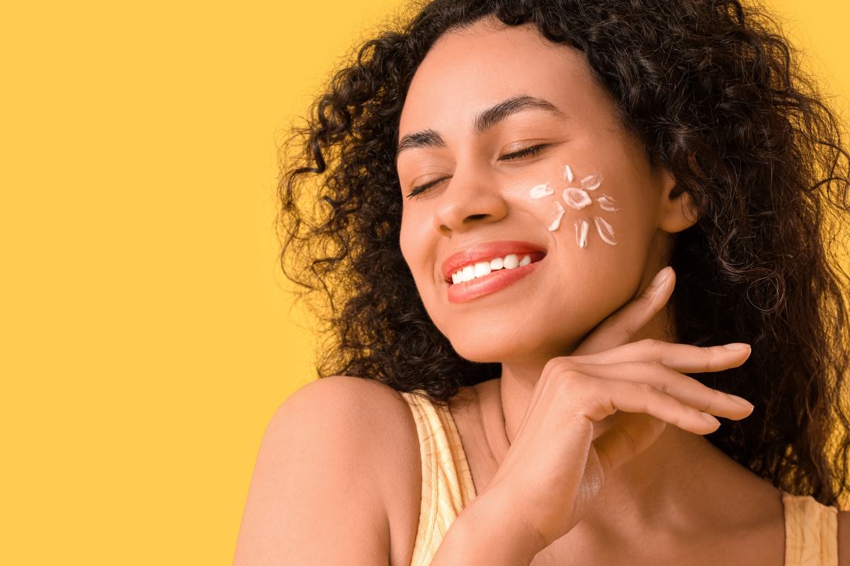Young African American woman with sun made of sunscreen cream on yellow background
