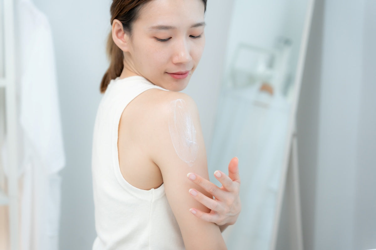 Young woman applying lotion to her shoulder in a clean, bright bathroom