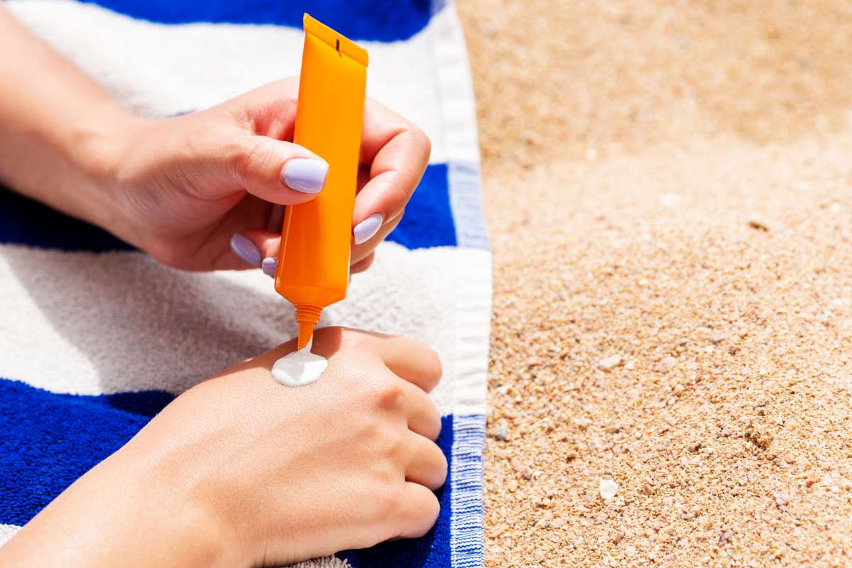 Attractive woman lying on a striped towel at the beach and squeezing sunblock from a tube on her hand